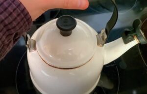 A hand carefully lifts the lid of a white kettle