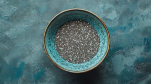 A blue ceramic bowl filled with chia seeds, placed on a textured teal background