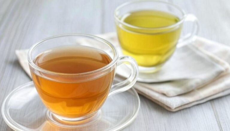 Two cups of tea, one brown, one green, sit on a light gray surface