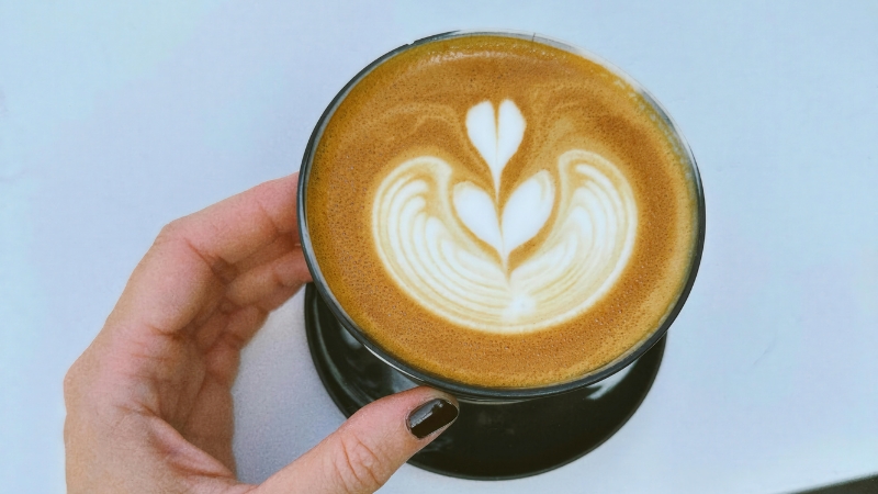 A hand holds a cup of latte with heart-shaped foam art