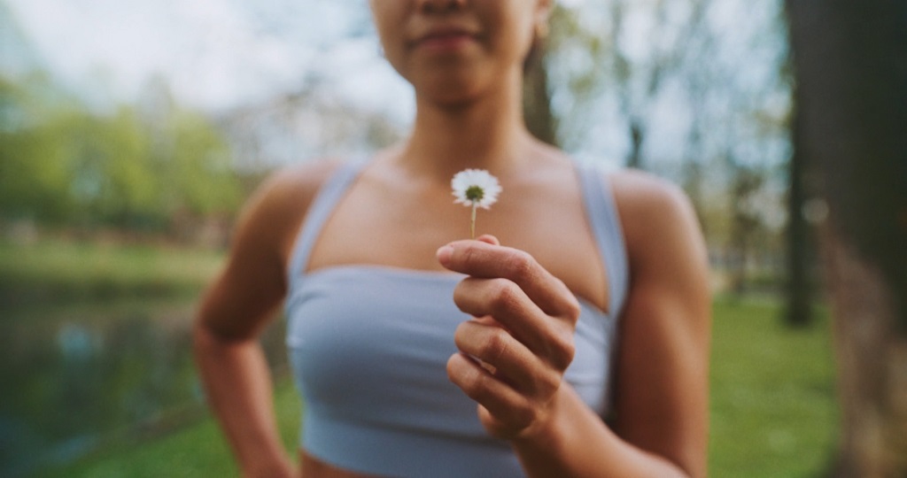 Woman in a sports bra outdoors holding a small chamomile flower between her fingers