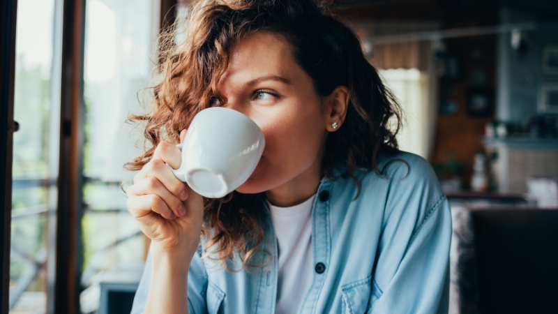 A woman sips coffee from a white cup, reflecting the hour by hour journey of caffeine effects