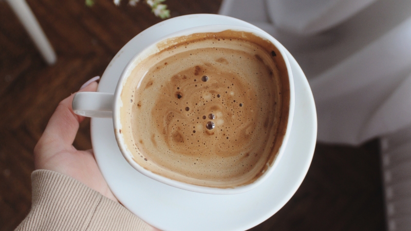 A person holds a cup of coffee, illustrating the question of how long caffeine stay in your system