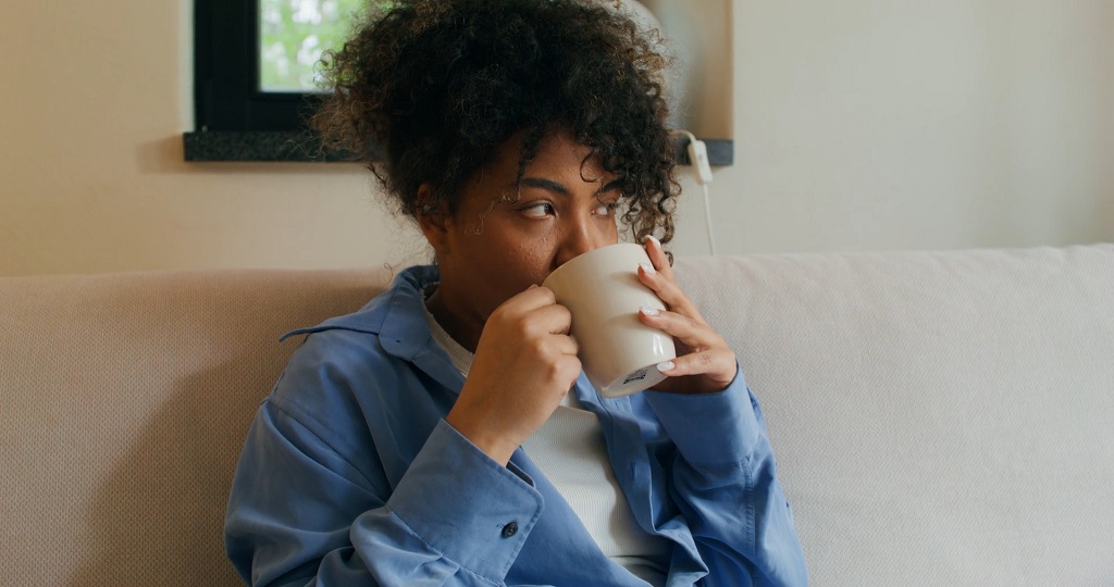 Pregnant woman sitting on a couch, drinking tea from a white mug, representing moderation and lifestyle choices during pregnancy