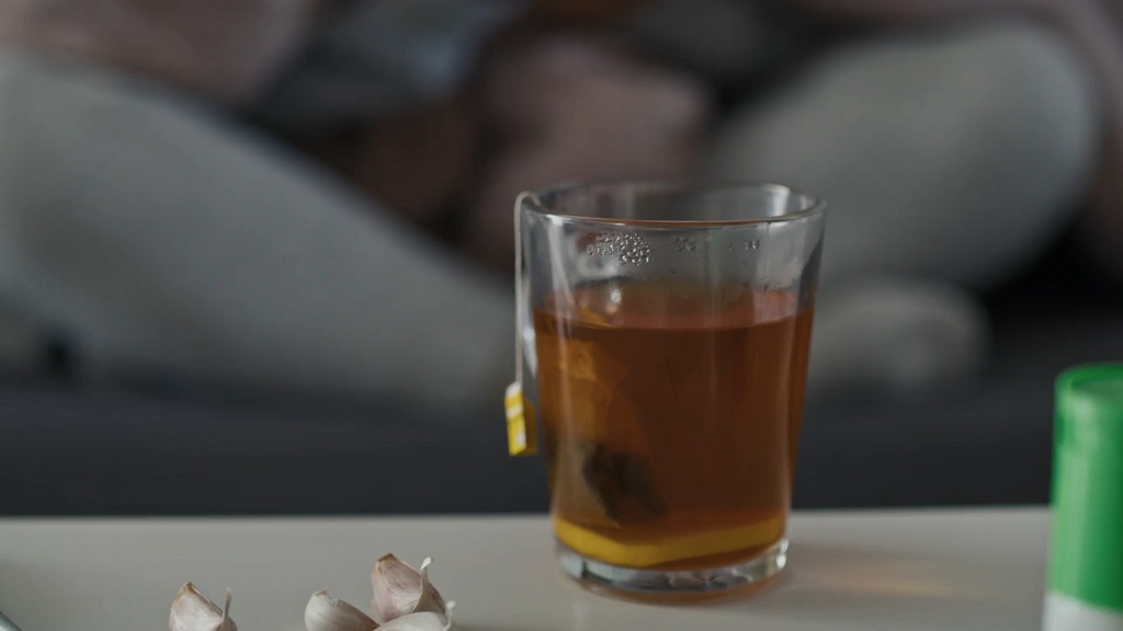Glass cup of herbal tea with a tea bag and slice of lemon, placed on a table with garlic cloves nearby